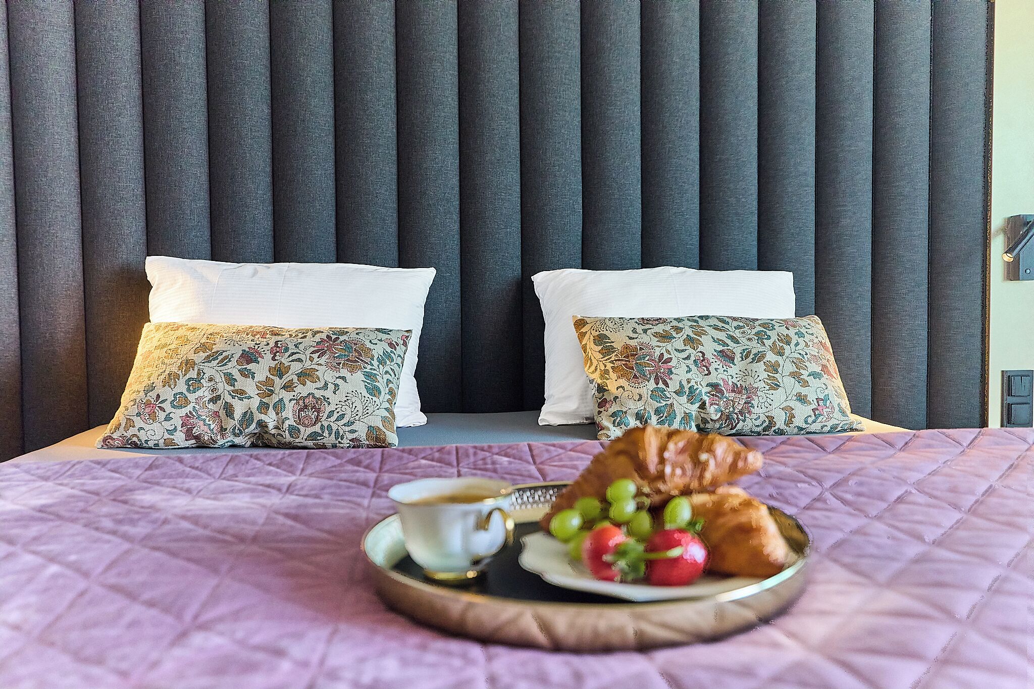 A bed with a headboard, two pillows, a plate with food and drink, and a blanket.