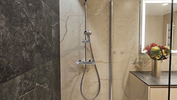 A modern bathroom with a glass-enclosed shower, a marble-tiled wall, and a vanity with a mirror and vase. - Baltic Infinity (Międzyzdroje)