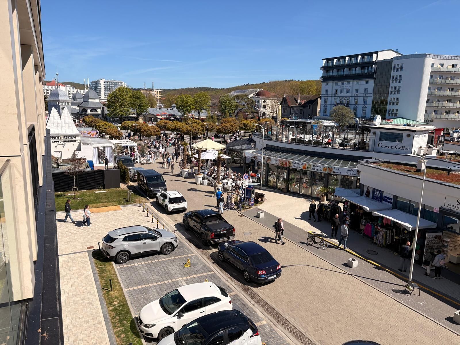 Une rue animée en milieu urbain, bordée de voitures garées, de piétons et de divers commerces.