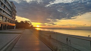 A waterfront promenade with a sunset view, a glass railing, and a modern building on the left. - Baltic Infinity (Międzyzdroje)