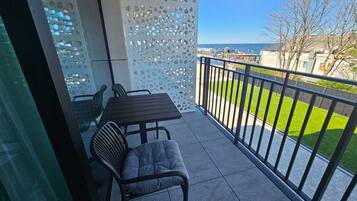 Un balcón con mesa y sillas, un muro decorativo perforado y vistas al mar y vegetación.