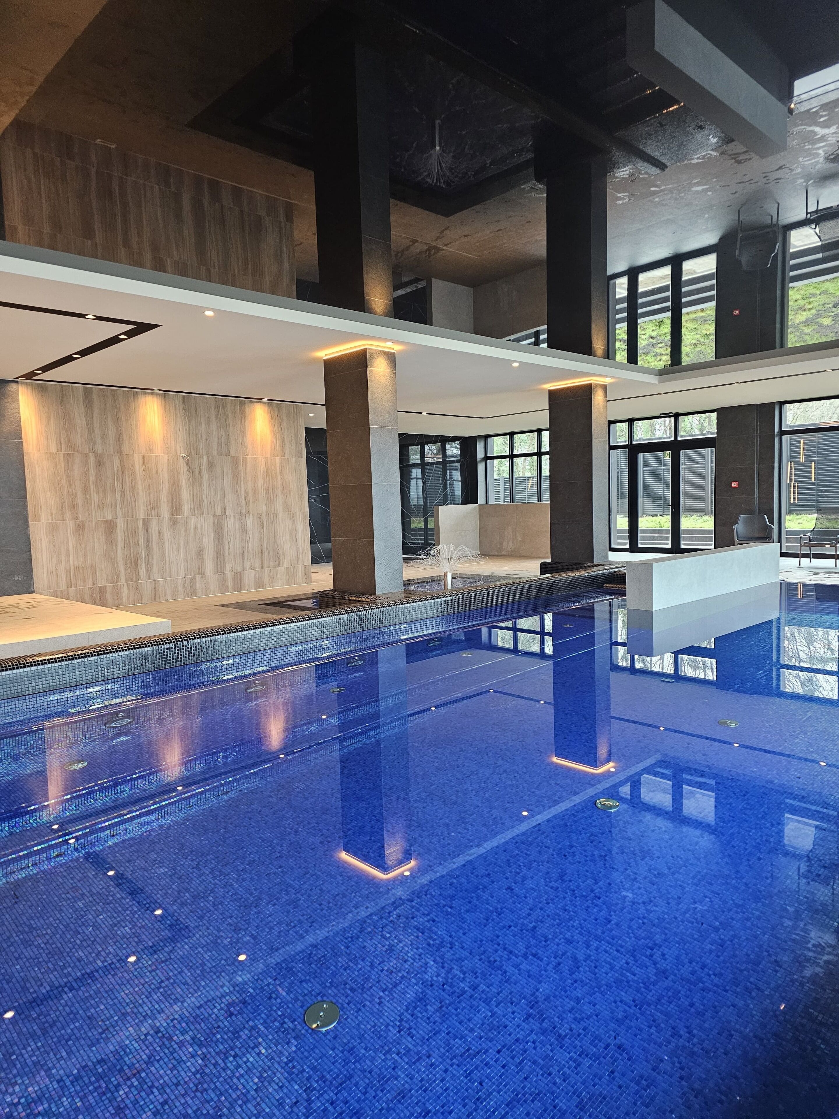 A modern indoor swimming pool with clear blue water, surrounded by high ceilings and large windows.