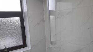 A bathroom with white marble tiles, a window, and a shower area. - Family- Near Lcy Airport- Sleeps 6- Parking- Wi-fi (Dagenham)