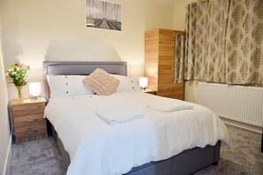 A neatly made bed with white linens and a single pillow, a wooden wardrobe, a nightstand with a lamp, and a framed picture on the wall. - Family- Near Lcy Airport- Sleeps 6- Parking- Wi-fi (Dagenham)