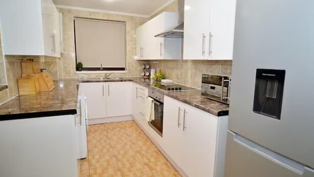 A modern kitchen with white cabinets, a granite countertop, and a built-in oven. - Family- Near Lcy Airport- Sleeps 6- Parking- Wi-fi (Dagenham)