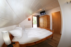Une chambre à coucher avec un lit en bois, une table de chevet avec une lampe, un téléviseur fixé au mur et une armoire.