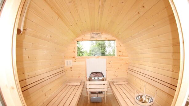 Uma sauna com paredes de madeira, uma janela, um banco e um balde.