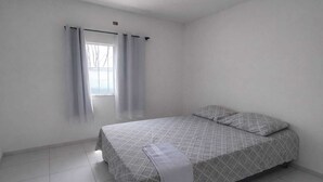 Ein schlichtes, sauberes Schlafzimmer mit Bett, Vorhängen und Fenster.