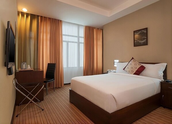 Una camera d'albergo con un letto grande, una scrivania con una sedia, una televisione e una finestra con tende.