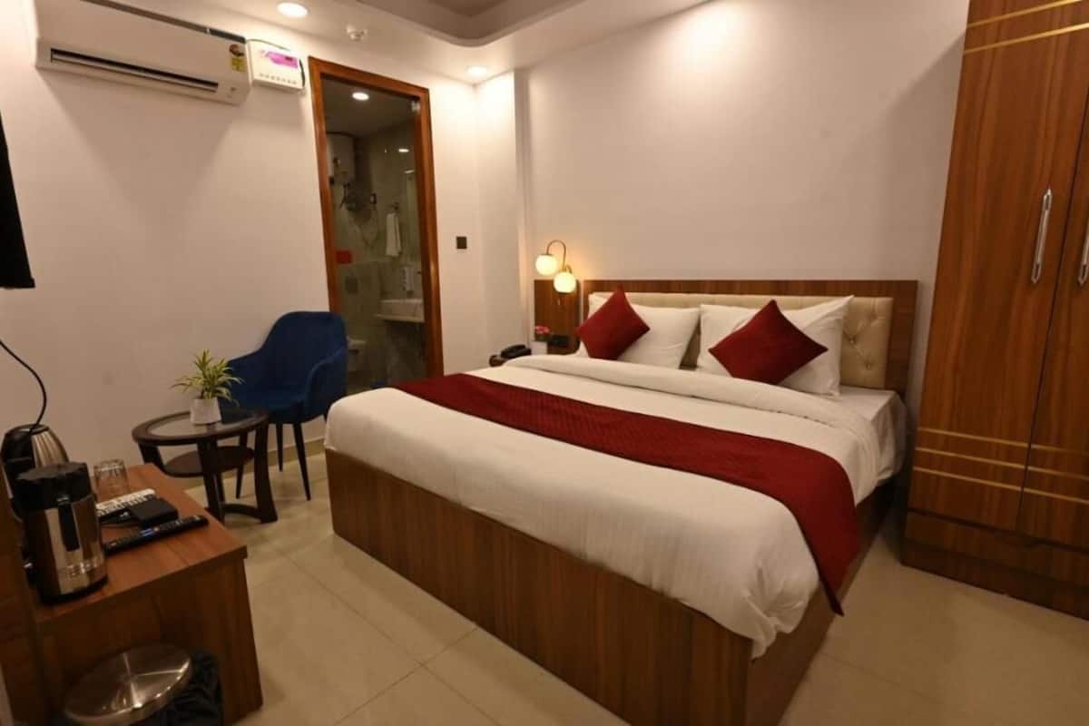 Habitación de hotel con una cama grande, mesita de noche y un escritorio con silla. Hay un armario y una pequeña mesa con una planta.