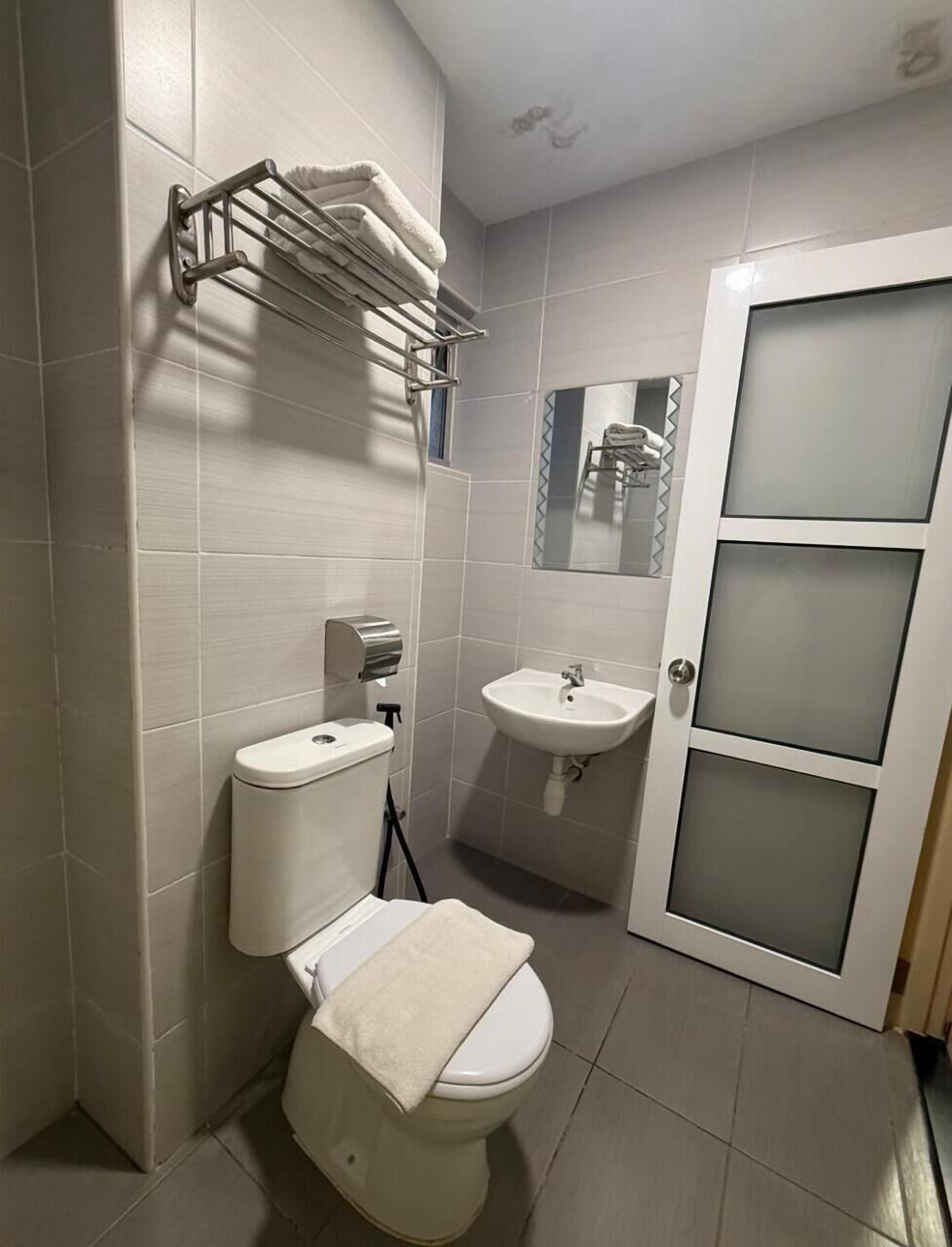 A bathroom with a toilet, sink, towel rack, and a frosted glass door.