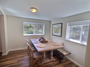 A dining area with a wooden table, chairs, and a bench. There are two windows with blinds, a ceiling light, and a framed butterfly picture on the wall. - Sky Blue 2Bdrm Guest House | Country Escape | Minutes to Beaches & Wineries (Arroyo Grande)