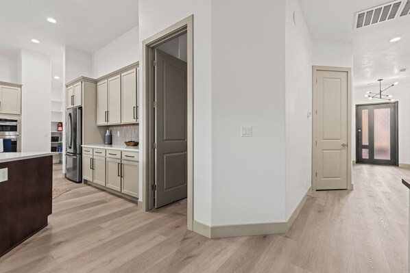 Une cuisine moderne avec des meubles blancs, un réfrigérateur en acier inoxydable et un plancher en bois.
