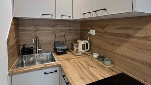 Eine kleine Küche mit weißen Schränken, einer Edelstahl-Spüle, einer schwarzen Induktionskochplatte und Holz Arbeitsplatten.
