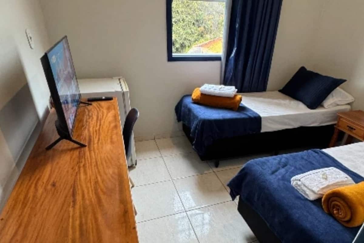 A bedroom with two beds, a desk, a computer, and a window with curtains.