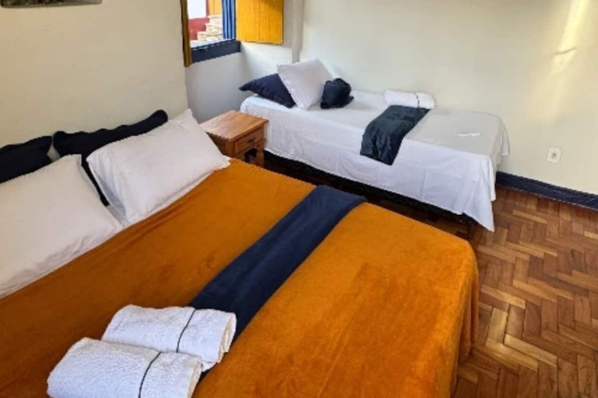 A hotel room with two beds, wooden flooring, and a window with blinds.