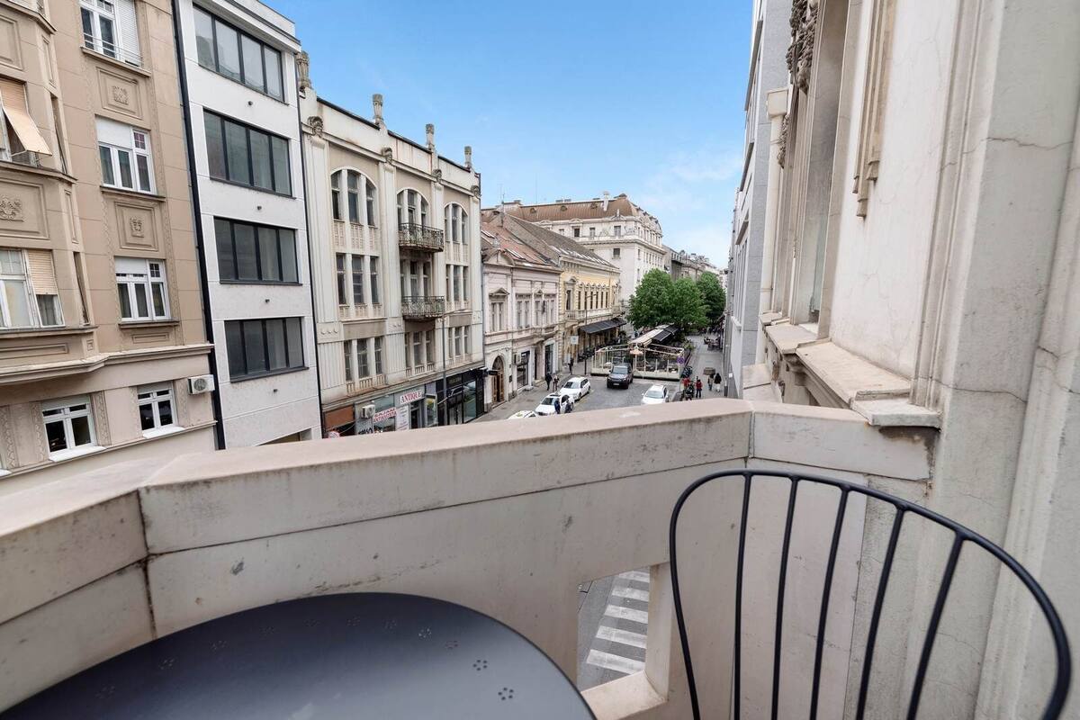 Un balcón con vistas a una calle bordeada de edificios, una silla y una mesa.