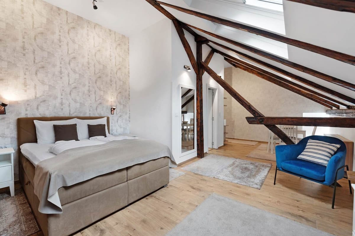 Un dormitorio con una cama, una mesita de noche, un sillón azul y una escalera que sube a un nivel superior.