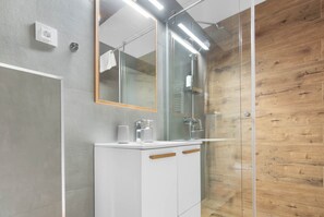 A modern bathroom with a glass shower enclosure, a white vanity with a mirror, and a wooden wall panel.