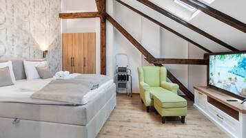 Een slaapkamer met een bed, een groene fauteuil, een televisie en een houten garderobe.