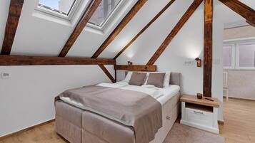 A bedroom with a sloped ceiling, wooden beams, a bed, bedside table, and a window.