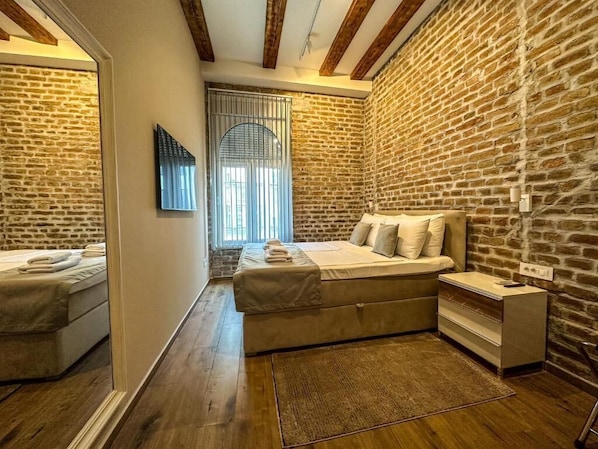 A bedroom with a large bed, a smaller bed, a nightstand, a mirror, and a window with blinds.