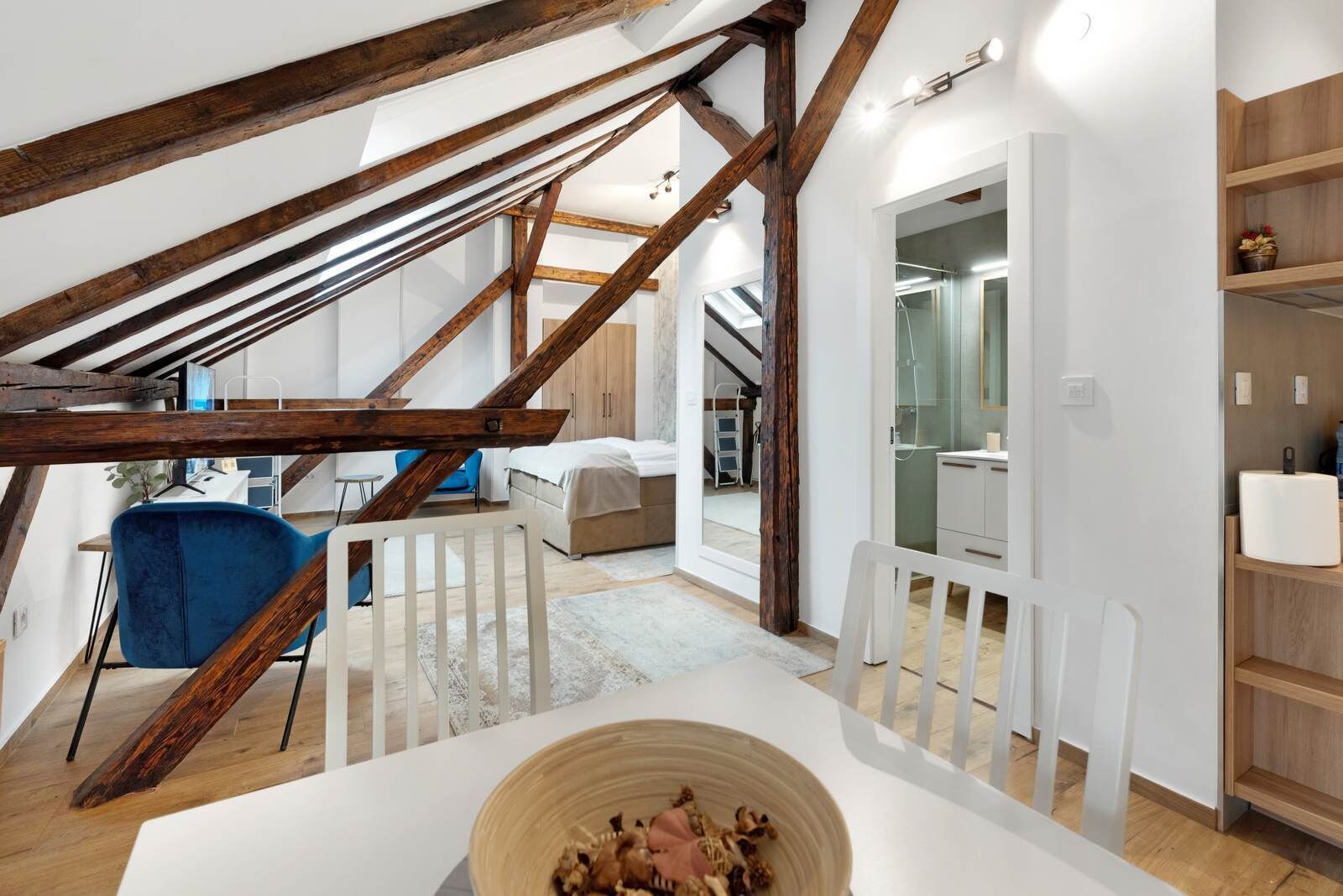 Un dormitorio tipo loft moderno con vigas de madera a la vista, una cama grande, un escritorio y un baño con ducha de vidrio.