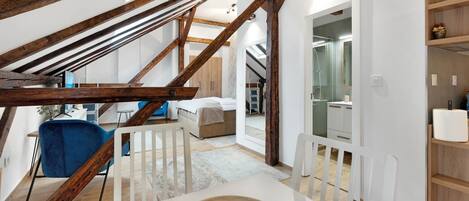 Un dormitorio tipo loft moderno con vigas de madera a la vista, una cama grande, un escritorio y un baño con ducha de vidrio.
