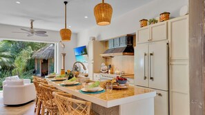 A modern kitchen with a central island, white cabinetry, and a dining area with wicker chairs. - **CASA DEL MONO @ MIDTOWN** Stunning Private Home & Pool + LAST KEY SERVICES… (Key West)