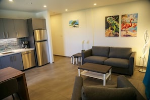 Ein modernes Wohnzimmer mit grauem Sofa, einem Couchtisch und einer Küchenzeile mit Edelstahlkühlschrank und Geschirrspüler.