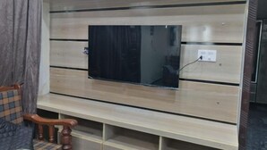 A wall-mounted TV with a wooden panel design, a power outlet, and a wooden bench below. - Navid’s Holiday Resort and Hotel, Murree – Spacious Three-Bedroom Apartment (Ghora Gali)