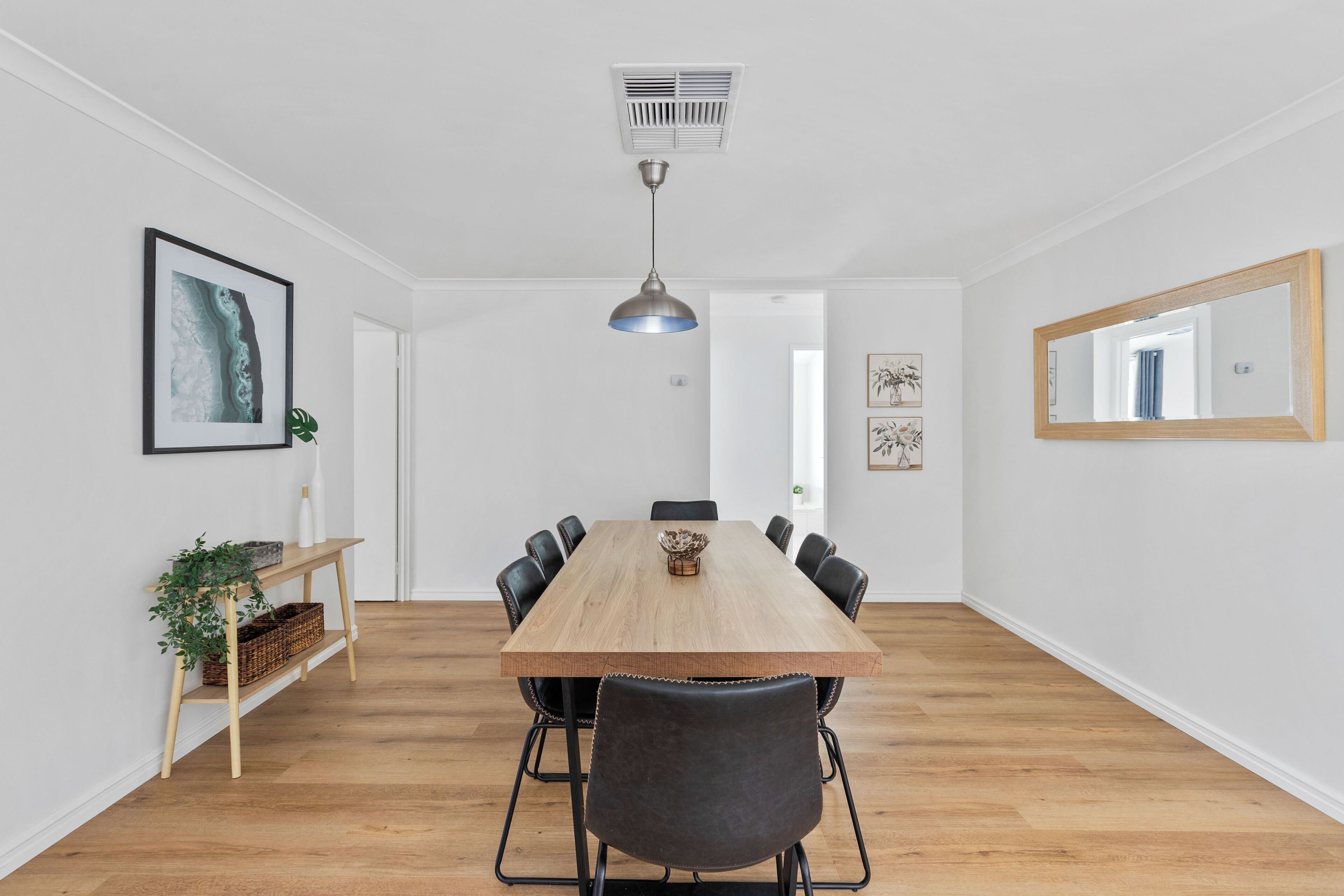 A dining area with a wooden table, black chairs, a pendant light, and a wall-mounted mirror.