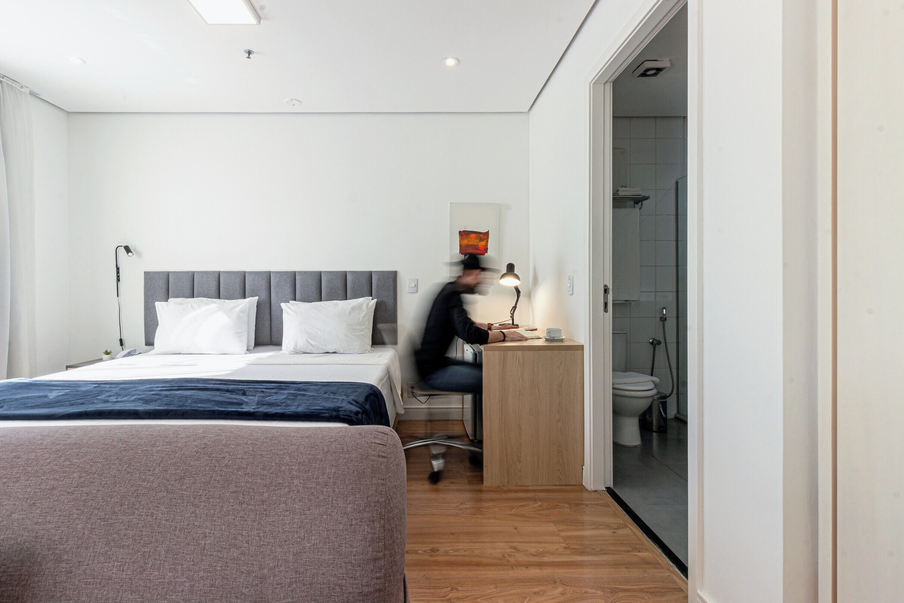 Et hotelværelse med en seng, et skrivebord og et badeværelse, der kan ses gennem en åben dør.