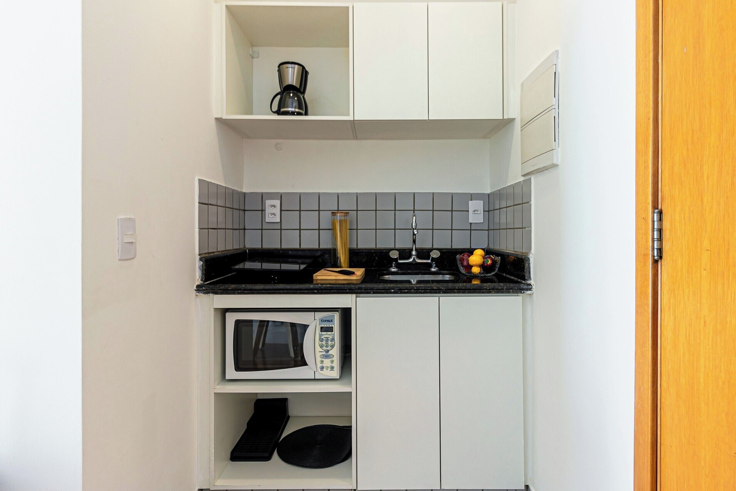 Una cocina compacta equipada con microondas, cafetera y lavamanos.