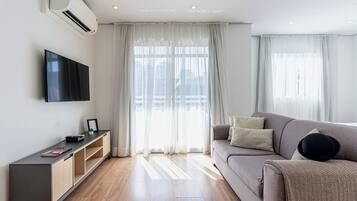 Un salon moderne avec un téléviseur à écran plat, un canapé gris et un plancher en bois.