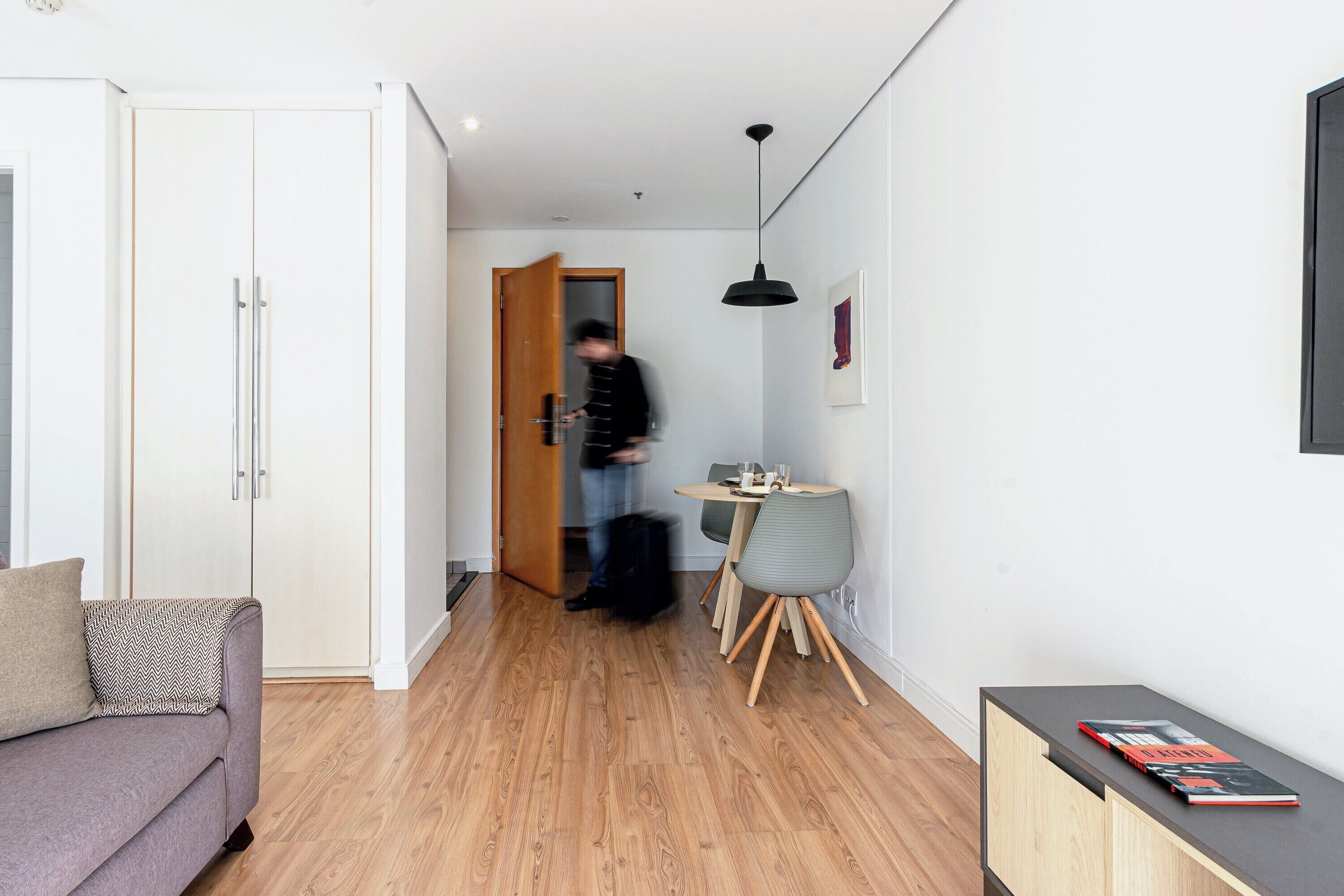 A modern living space with a sofa, a dining table with chairs, and a small cabinet with books.