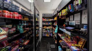 A narrow aisle in a convenience store with shelves stocked with snacks, drinks, and other items. - St. Charbel by Charlie (São Paulo)