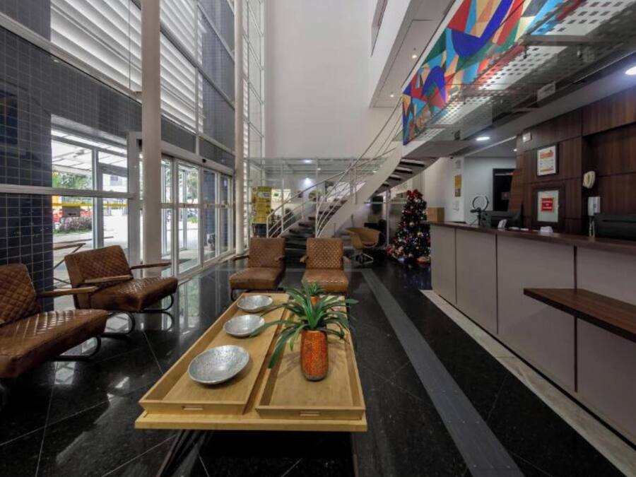 A modern hotel lobby with a reception desk, seating area, and a staircase.