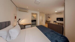 Een hotelkamer met een bed, bureau, stoel, televisie en een kleine kitchenette.