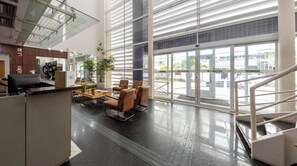 A spacious lobby with a reception desk, seating area, and large windows offering views of the outside. - St. Charbel by Charlie (São Paulo)