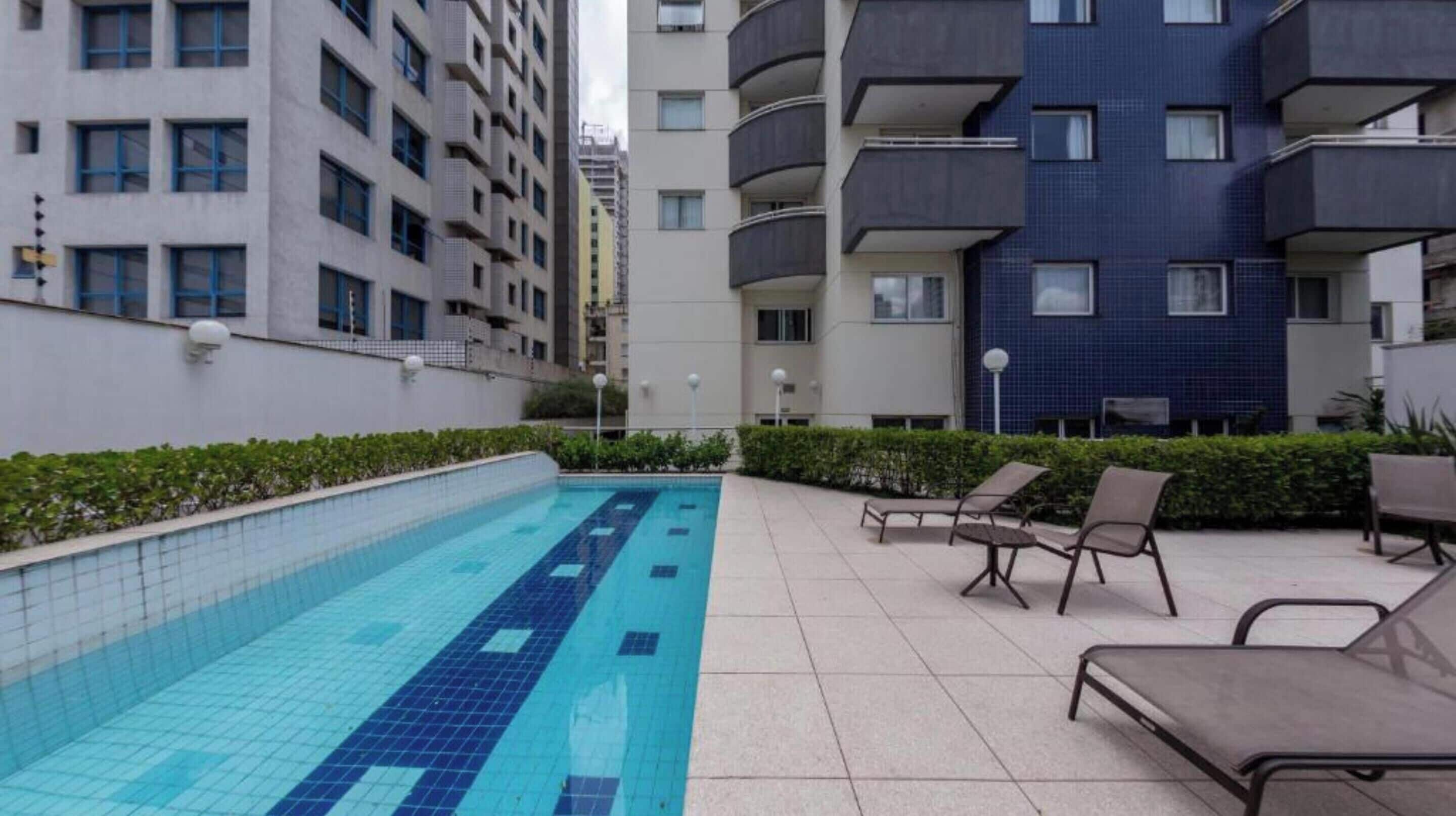 A swimming pool with tiled flooring, surrounded by lounge chairs and a low hedge.