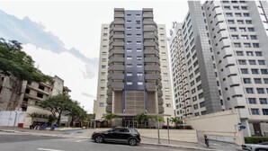 A modern high-rise building with a central atrium, multiple balconies, and a parking area in front. - St. Charbel by Charlie (São Paulo)