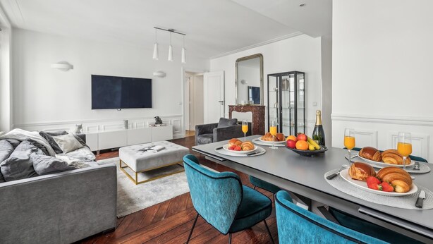 Un salon moderne avec un canapé, un pouf et un coin repas où l’on prend le petit-déjeuner.