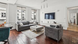 Un salon moderne avec un canapé d’angle, un pouf et un téléviseur fixé au mur.