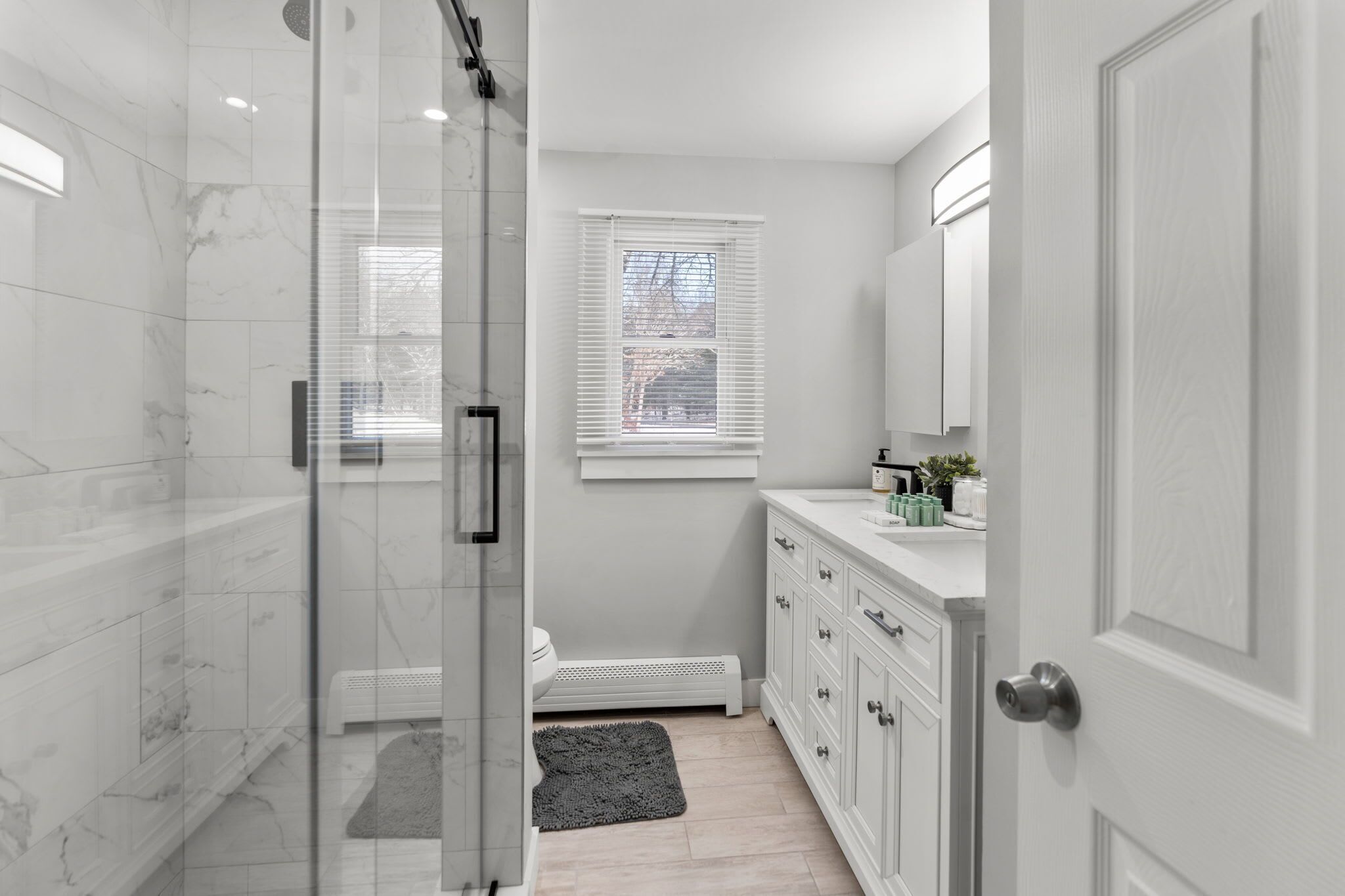 A modern bathroom with a glass shower enclosure, a white vanity with a sink, and a window with blinds.
