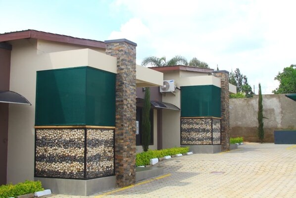 A row of modern buildings with green and beige facades, stone pillars, and a paved walkway.