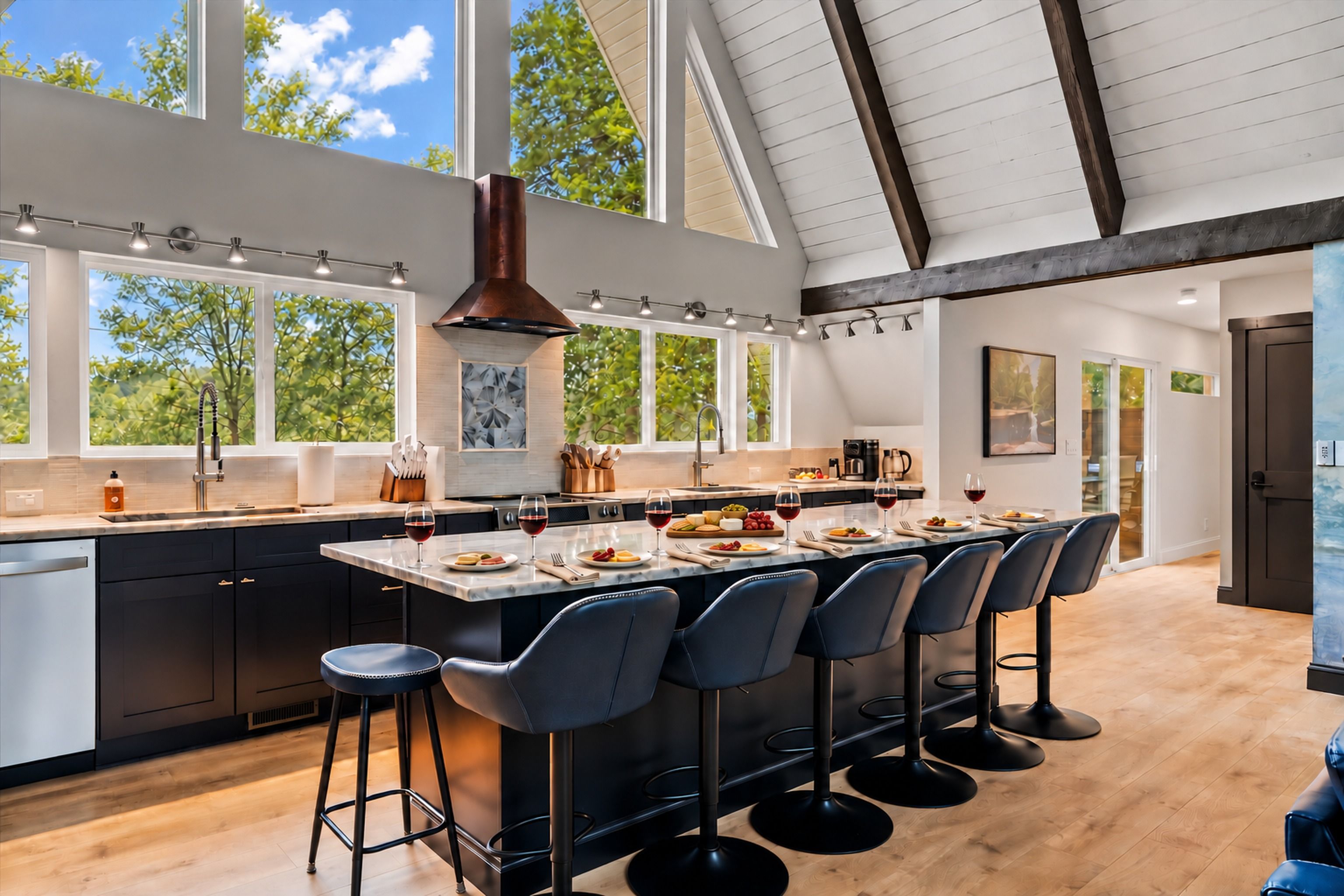 A modern kitchen with a large island, bar stools, and a view of trees through the windows.