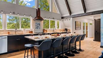 A modern kitchen with a large island, bar stools, and a view of trees through the windows.