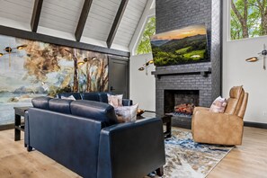 A modern living room with a fireplace, leather sofas, and a large TV mounted on the wall.
