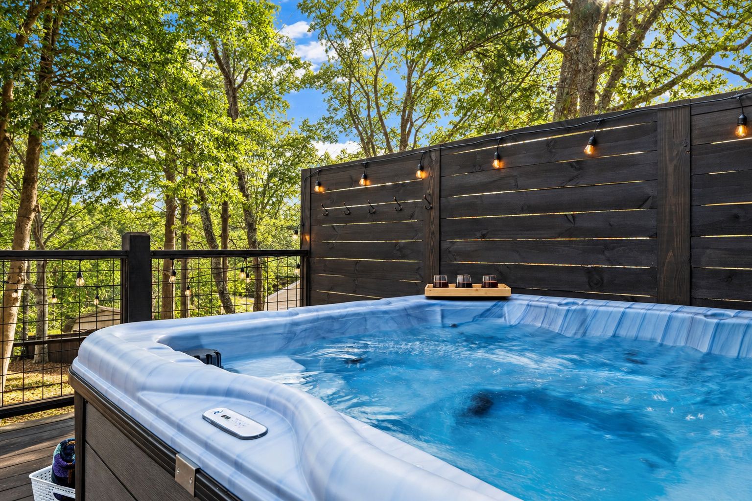 A hot tub with a wooden deck and a wooden fence, surrounded by trees.